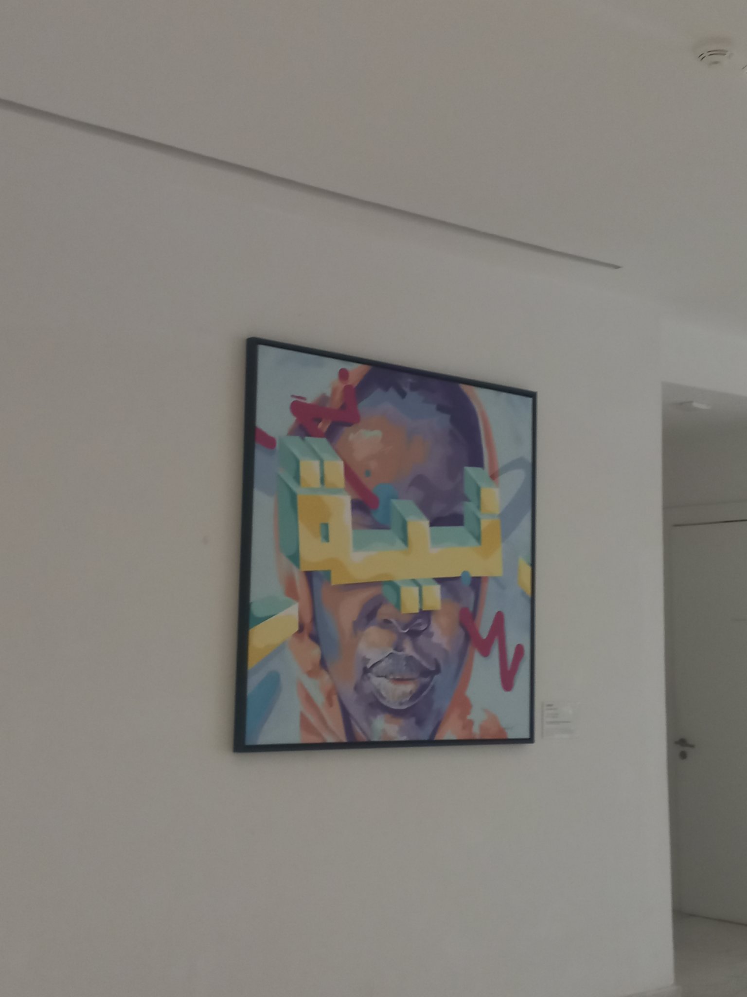 Framed painting: bold three-dimensional Arabic calligraphy in yellow and teal spelling Nia, layered over an expressive portrait in violet and ochre with magenta gestural marks.